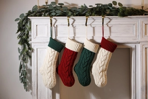 Four knitted Christmas stockings in red, white and green hanging on a decorated fireplace