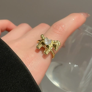 Detail of a golden horse ring with a heart-shaped zircon worn on the index finger