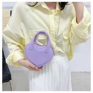 Detail of purple heart-shaped jelly bag with gold chain strap on light yellow shirt