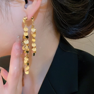 Vue détaillée de longues boucles d'oreilles pompons dorés avec disques sur un modèle