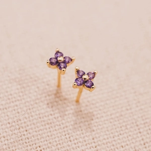 Macro shot of gold four-leaf flower studs featuring inlaid purple zircons on fabric