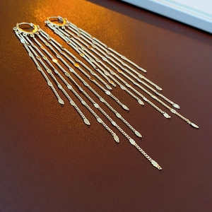 Close-up of gold chain fringe earrings with metal leaf charms on a textured background