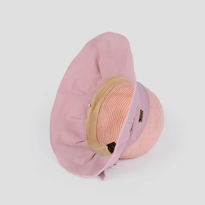Detailed close-up of pink sun hat featuring woven straw texture and metal logo plate