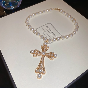 Detailed close-up of hollow gold cross pendant with pearls on an elegant display card