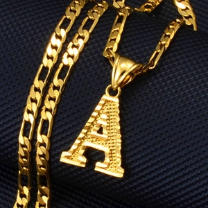 Close-up of golden letter A pendant on a classic Figaro chain against navy blue background