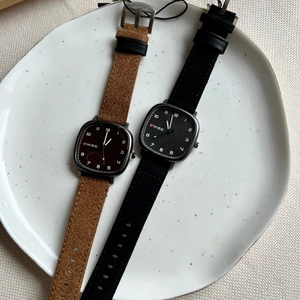 Close-up of square black quartz watches with brown and black suede straps on a plate