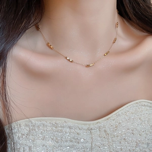 Close-up of gold bead necklace with small cubes on a woman neck over white dress