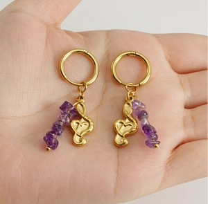 Detail of 18k gold note hoop earrings with natural purple stone on a palm