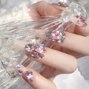 Sparkly press-on nails with large pink and blue rhinestones on a nude base color