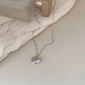 Detailed close-up of polished silver heart pendant necklace on cozy knit texture
