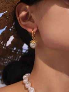 Detail of 18k gold plated floral cap earrings with large silver-grey pearls on a model