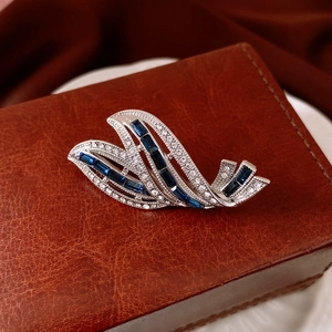 Macro shot of silver swan brooch with blue gems and white zircons on leather box