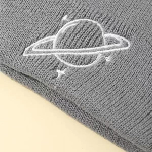 Close-up of grey knit beanie featuring white embroidered planet logo on the folded cuff