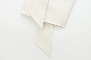 Nahaufnahme eines cremeweißen Satintops mit eleganten Schalgurten und feinem Glanz
