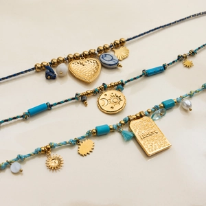 Close-up of turquoise beads, gold heart and sun-moon pendants on layered woven bracelets