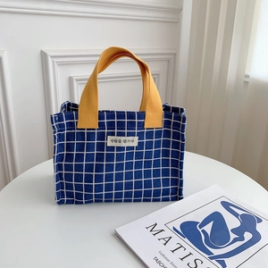 Close-up of blue checkerboard canvas lunch bag with yellow handles and woven label