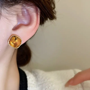 Macro view of square amber gemstone stud earrings plated in 18K gold on model's ear
