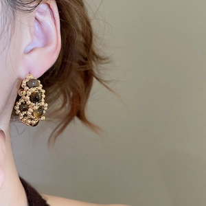 Detail of model wearing C-shaped gold earrings set with dark tiger eye beads