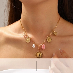 Detail of a vintage gold necklace featuring a sun disc, pink heart, and pearl charms