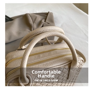 Close-up of thick round handles and double metal zippers on beige woven Boston bag
