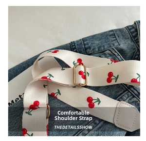 Detail of adjustable cream fabric shoulder strap with red cherry print and metal buckle
