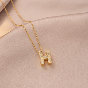 Macro detail of gold-plated H letter pendant with pavé zircon on champagne silk fabric