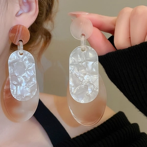 Vue macro de grandes boucles d'oreilles en résine marbrée blanche et ambre sur modèle