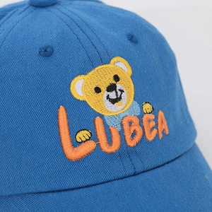 Close-up of embroidered yellow bear and LUBEA letters on blue baby baseball cap