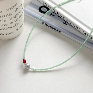 Collier de perles minimaliste avec perles vertes et agate rouge sur fond blanc pur