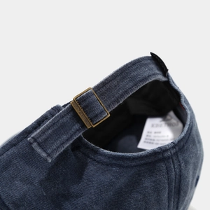 Detail of navy blue baseball cap featuring adjustable bronze buckle and cotton fabric texture