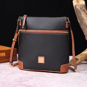 Detail of black pebble leather crossbody bag featuring brown trim and gold-tone metal plate