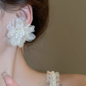 Detail of a white mesh flower earring featuring layered fabric petals and a center bead