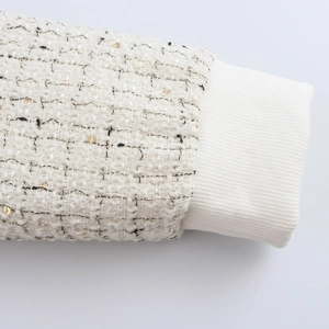 Détail de la manche d'une veste en tweed blanc avec paillettes dorées et poignets côtelés