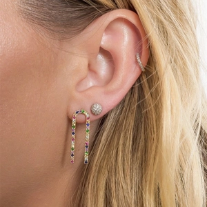 Macro shot of U-shaped gold earrings with colorful zircon stones on model's ear