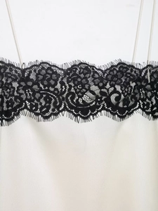 Detail of white satin camisole featuring intricate black lace trim and eyelash edges