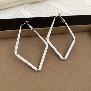 Close-up of silver geometric rhombus pendant hoop earrings on a velvet jewelry tray