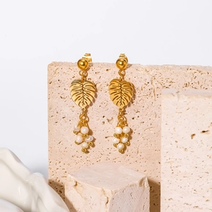 18K gold plated leaf earrings with white pearls displayed on minimalist stone props