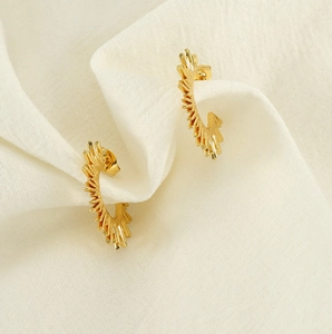 Macro detail of golden fan-shaped sunflower earring with serrated edges on white fabric