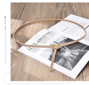 Detailed view of light brown skinny waist belt tied in a minimalist knot over a magazine