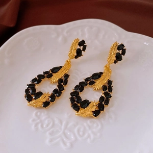 Detailed close-up of gold leaf-shaped earrings with black gemstones on a white tray