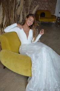Detail of white deep V-neck bridal gown featuring sequin texture and long cuffed sleeves