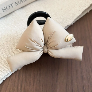 Detail of cream bow hair claw with gold metal tag and soft padded fabric texture