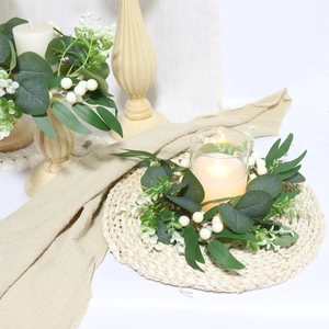 Dettaglio di una ghirlanda per candele con eucalipto e bacche bianche su runner beige
