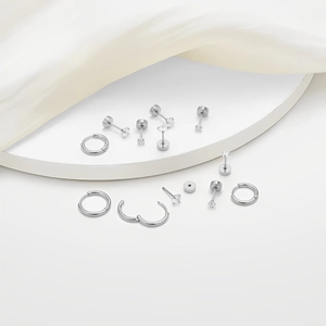 Detail view of silver round stud earrings and hoops set on white silk fabric background