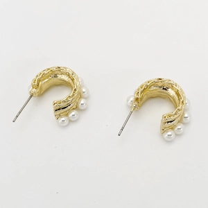 Detailed close-up of golden C-shaped hoop earrings with small white pearls on a white surface
