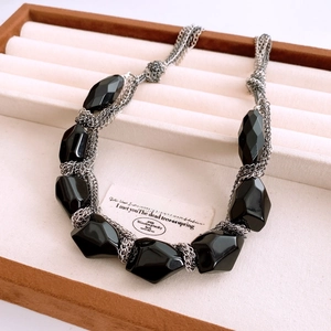 Macro view of multi-layer gold chain necklace with black acrylic faceted oval pendants
