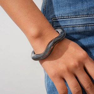 Detail view of wavy smoky gray acrylic bracelet worn with casual denim outfit