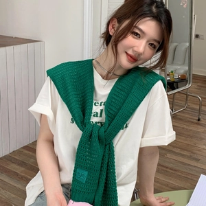 Detail of green knit shawl with DD logo tag draped over a white printed t-shirt