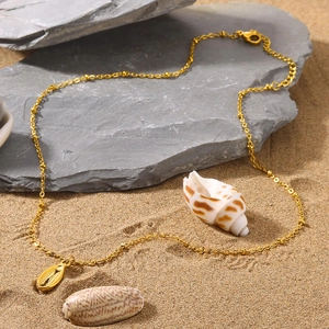 Detail of golden stainless steel necklace with shell pendant on a beach setting