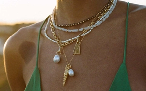Detail of layered gold necklaces with shell and pearl pendants worn on a female model